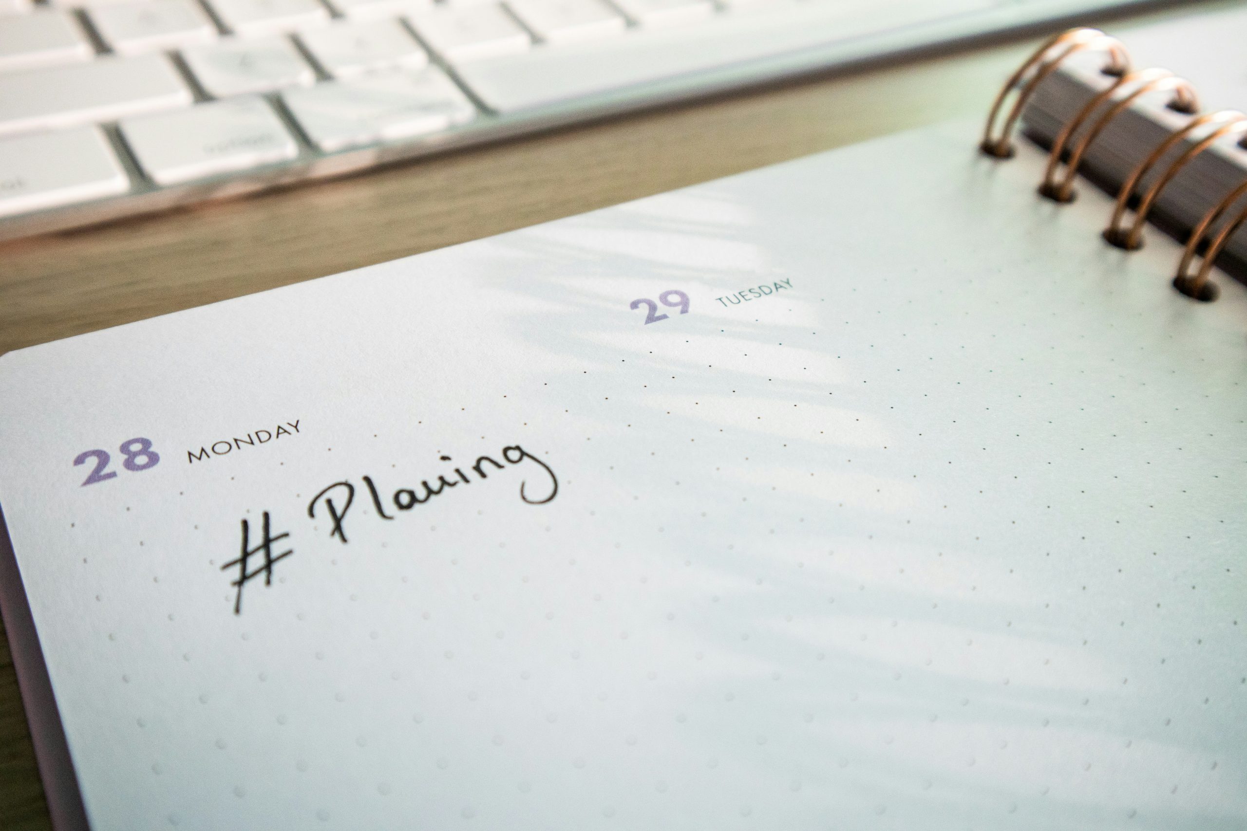 Desk with a keyboard and a planner with the hashtag #planning on it